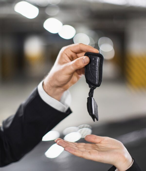 Caucasian businessman in suit handing car keys to Caucasian woman in underground parking, symbolizing car sale or rental transaction.